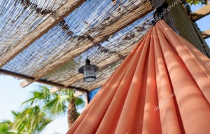 A red hammock hangs in the shade of a porch in summer.